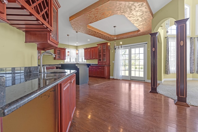 kitchen with pendant lighting, dark hardwood / wood-style floors, a kitchen island, a kitchen breakfast bar, and a raised ceiling