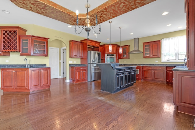 kitchen with decorative light fixtures, wall chimney exhaust hood, dark wood-type flooring, appliances with stainless steel finishes, and a center island