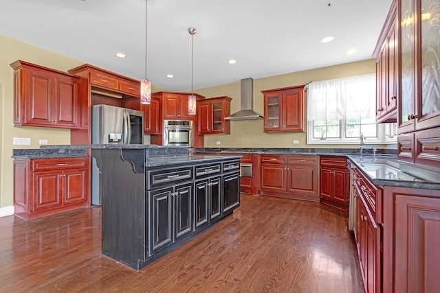 kitchen featuring stainless steel appliances, decorative light fixtures, a center island with sink, dark hardwood / wood-style floors, and wall chimney range hood