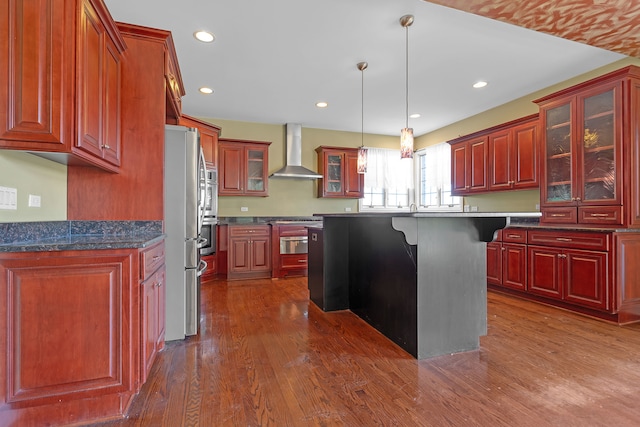 kitchen with wall chimney exhaust hood, a kitchen island, a breakfast bar area, decorative light fixtures, and dark hardwood / wood-style floors