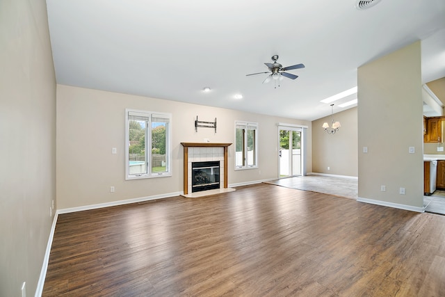 unfurnished living room with ceiling fan with notable chandelier, a tiled fireplace, and dark hardwood / wood-style floors