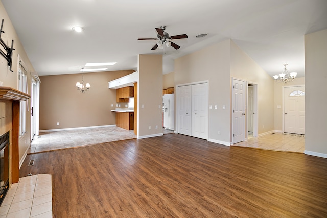 unfurnished living room with light wood-type flooring, ceiling fan with notable chandelier, a fireplace, and lofted ceiling