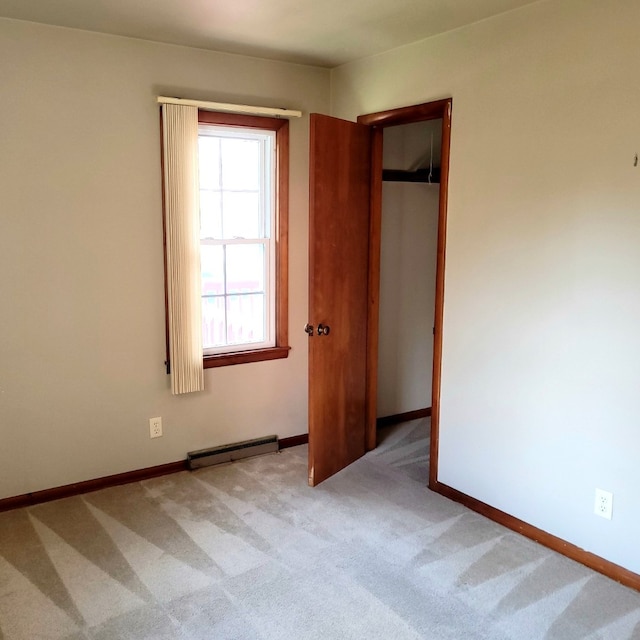 unfurnished bedroom with light carpet, a closet, and a baseboard heating unit