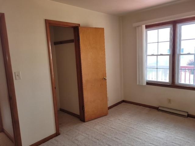 unfurnished bedroom featuring light carpet, a baseboard heating unit, and a closet