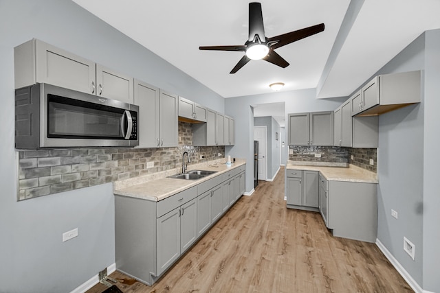 kitchen with gray cabinets, light wood-type flooring, tasteful backsplash, sink, and ceiling fan