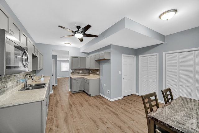 kitchen featuring decorative backsplash, gray cabinets, light wood-type flooring, ceiling fan, and sink