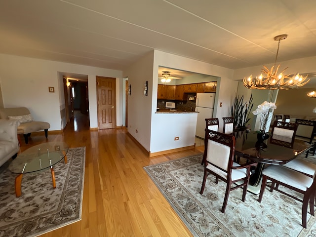 dining space with ceiling fan with notable chandelier and light hardwood / wood-style flooring