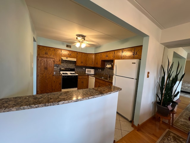 kitchen with ceiling fan, kitchen peninsula, white appliances, tasteful backsplash, and light hardwood / wood-style floors