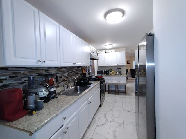 kitchen featuring white cabinets, sink, appliances with stainless steel finishes, light stone countertops, and decorative backsplash