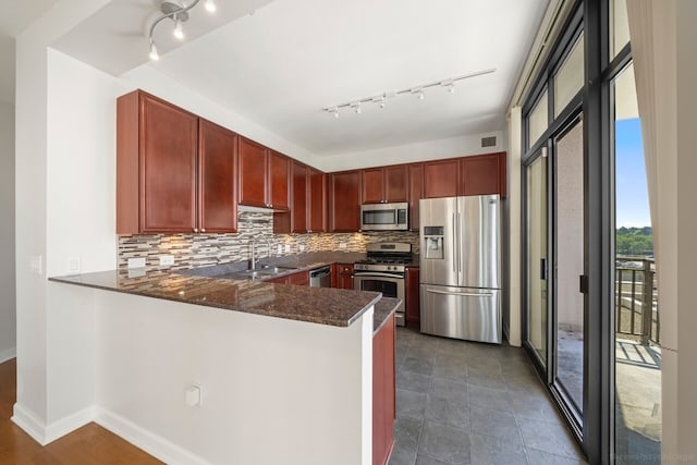 kitchen with track lighting, appliances with stainless steel finishes, kitchen peninsula, and tasteful backsplash