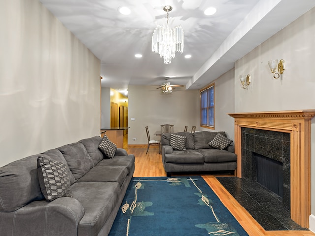 living room featuring wood-type flooring, ceiling fan with notable chandelier, and a tile fireplace