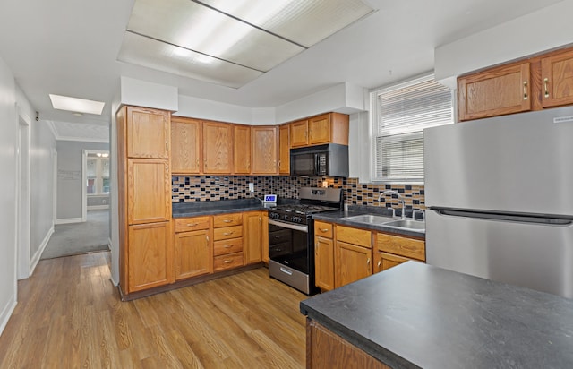 kitchen with light hardwood / wood-style floors, backsplash, stainless steel appliances, a skylight, and sink