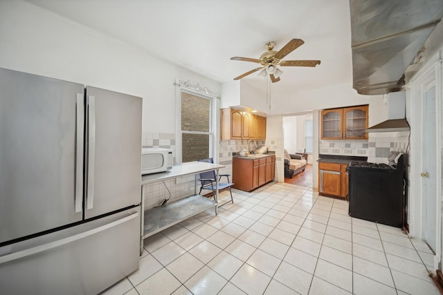 kitchen with stainless steel refrigerator, backsplash, light tile patterned floors, gas stove, and wall chimney range hood