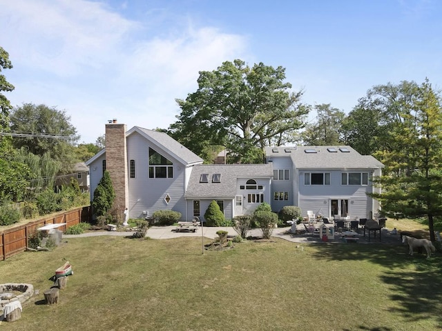 rear view of house featuring fence, a patio, a chimney, a shingled roof, and a yard