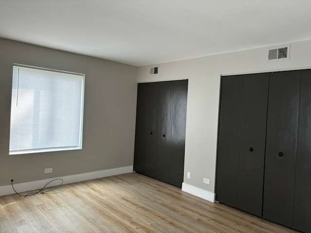 unfurnished bedroom with light hardwood / wood-style flooring and multiple closets