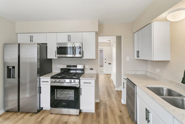 kitchen with light stone countertops, sink, stainless steel appliances, white cabinets, and light wood-type flooring