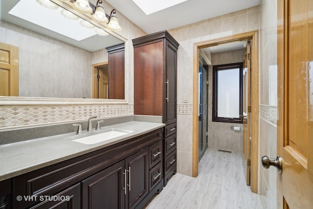 bathroom with vanity, tile walls, an enclosed shower, and a skylight