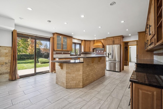 kitchen featuring premium range hood, a kitchen bar, dark stone counters, a center island, and stainless steel fridge with ice dispenser