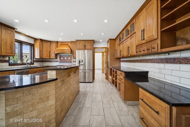 kitchen featuring premium range hood, appliances with stainless steel finishes, tasteful backsplash, sink, and dark stone countertops