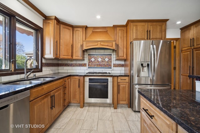 kitchen with premium range hood, sink, dark stone counters, stainless steel appliances, and decorative backsplash