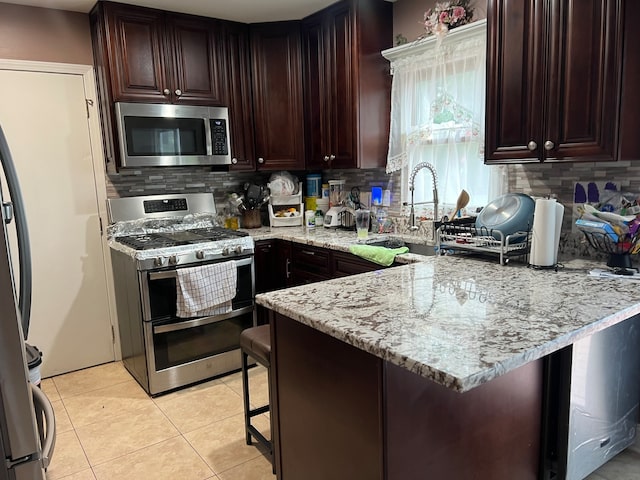 kitchen with appliances with stainless steel finishes, kitchen peninsula, a breakfast bar area, and light stone counters