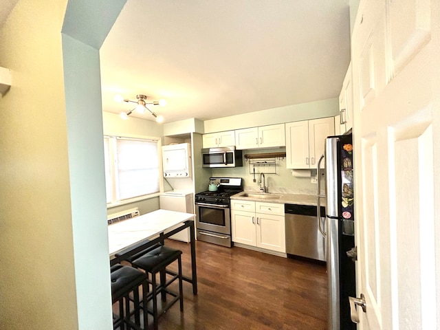 kitchen with sink, dark wood-type flooring, white cabinetry, appliances with stainless steel finishes, and stacked washer / drying machine