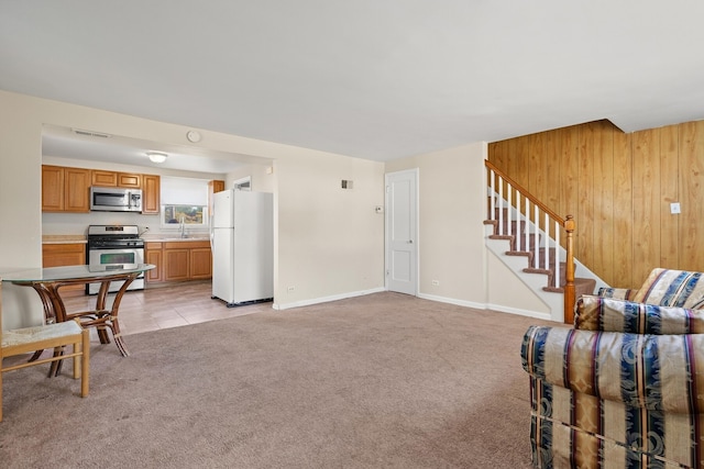 living room featuring wooden walls, sink, and light carpet