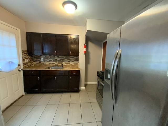 kitchen with appliances with stainless steel finishes, decorative backsplash, light tile patterned flooring, dark brown cabinets, and sink