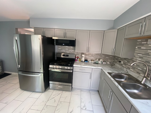 kitchen featuring appliances with stainless steel finishes, gray cabinetry, sink, and tasteful backsplash