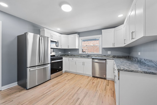 kitchen with sink, white cabinets, stone counters, light hardwood / wood-style flooring, and appliances with stainless steel finishes