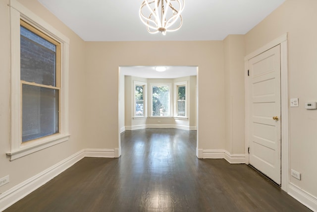 spare room featuring an inviting chandelier and dark hardwood / wood-style floors