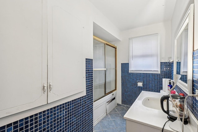 bathroom with tile patterned flooring, vanity, bath / shower combo with glass door, and tile walls