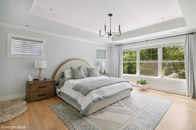 bedroom with an inviting chandelier, a tray ceiling, light wood-type flooring, and crown molding