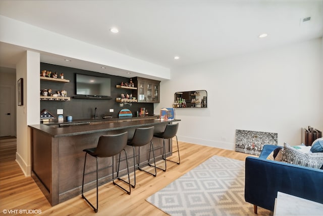 bar with dark brown cabinetry and light wood-type flooring