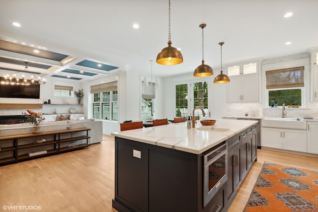 kitchen featuring light hardwood / wood-style floors, a kitchen island with sink, white cabinetry, decorative light fixtures, and light stone countertops