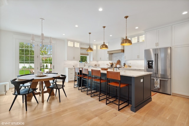 kitchen featuring high quality fridge, light wood-type flooring, white cabinetry, and a center island with sink