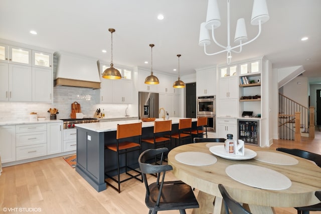 dining space featuring light wood-type flooring, beverage cooler, ornamental molding, sink, and a notable chandelier