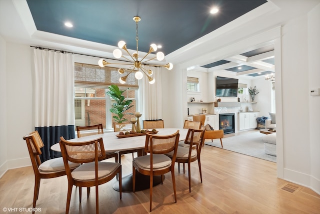 dining space with a raised ceiling, a high end fireplace, coffered ceiling, a notable chandelier, and light wood-type flooring