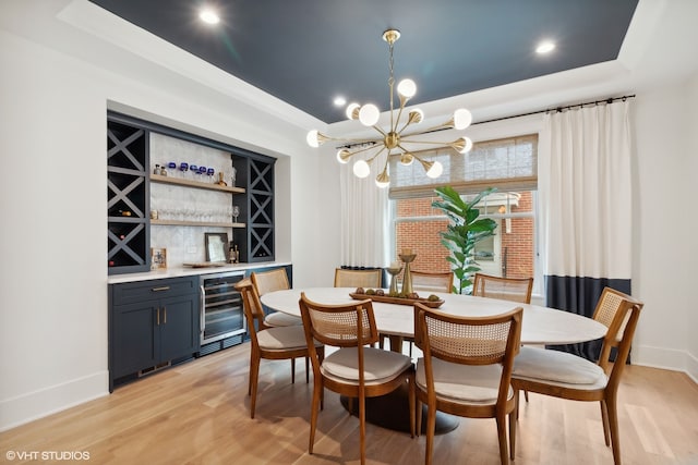 dining room featuring wine cooler, a tray ceiling, an inviting chandelier, light hardwood / wood-style flooring, and bar area