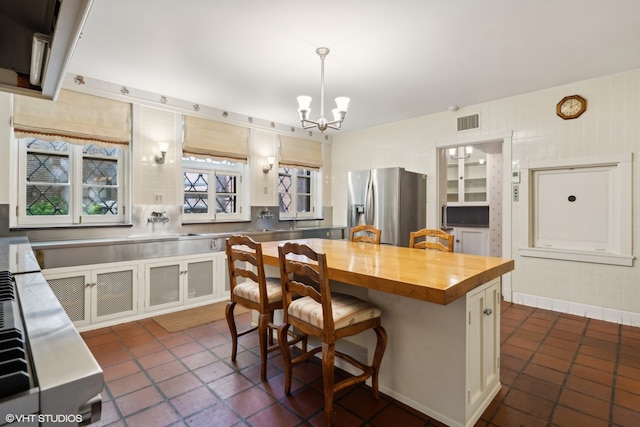 kitchen featuring hanging light fixtures, a kitchen bar, a center island, stainless steel refrigerator with ice dispenser, and wood counters