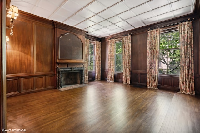 unfurnished living room featuring wooden walls, dark hardwood / wood-style floors, and plenty of natural light