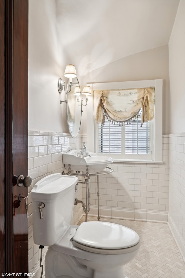 bathroom with tile walls, vaulted ceiling, sink, and toilet