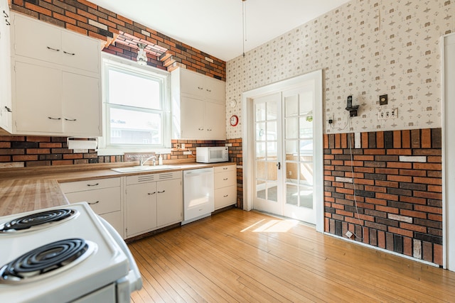 kitchen with brick wall, white cabinets, white appliances, light hardwood / wood-style flooring, and sink