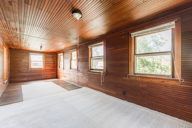 carpeted empty room featuring wood ceiling, wood walls, and plenty of natural light