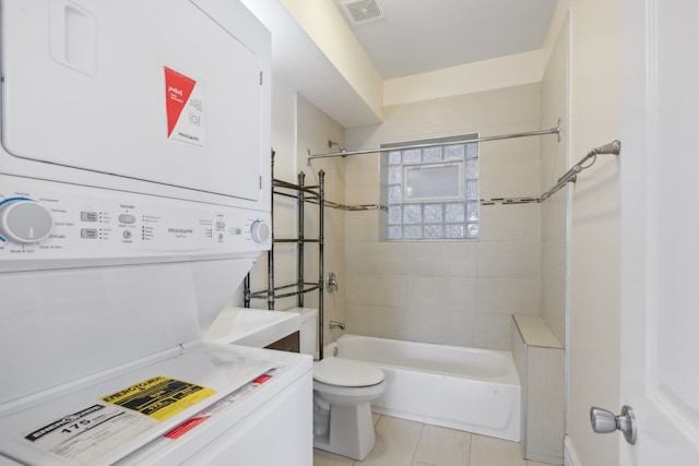 bathroom featuring tiled shower / bath, tile patterned floors, stacked washer / drying machine, and toilet