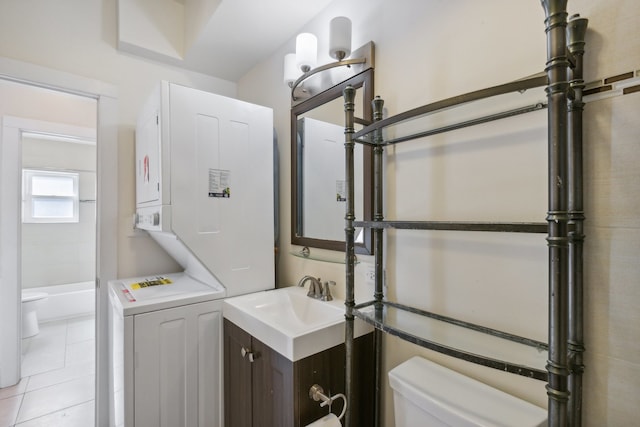 bathroom featuring stacked washer and clothes dryer, vanity, tile patterned flooring, and toilet