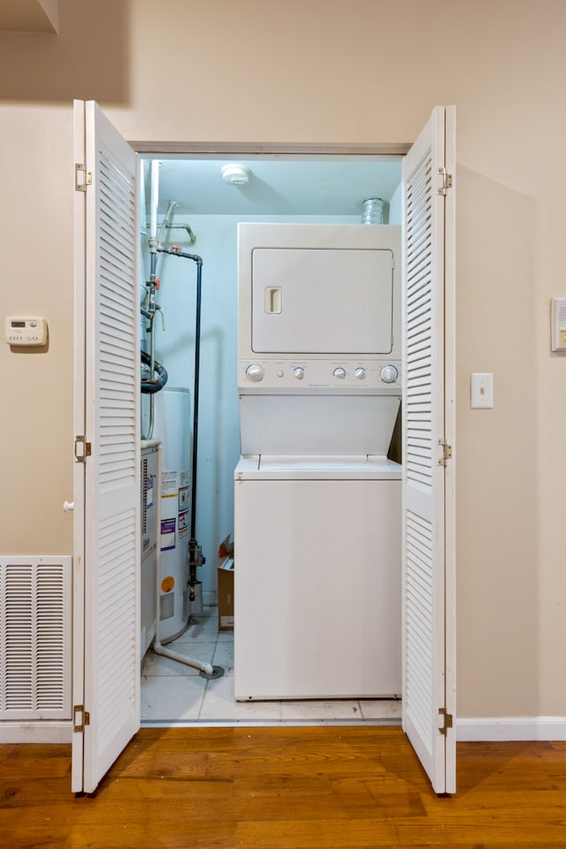 washroom featuring gas water heater, hardwood / wood-style flooring, and stacked washer / drying machine