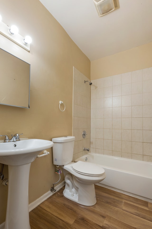 full bathroom featuring wood-type flooring, tiled shower / bath combo, and toilet