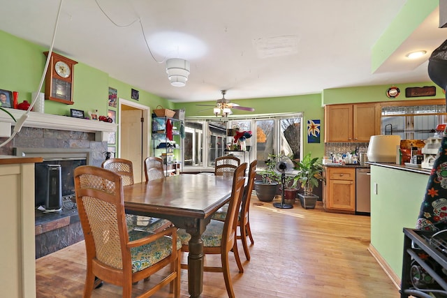 dining room with ceiling fan, a stone fireplace, and light wood-type flooring