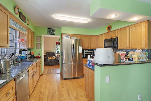 kitchen with stainless steel appliances, dark stone counters, light wood-type flooring, decorative backsplash, and sink